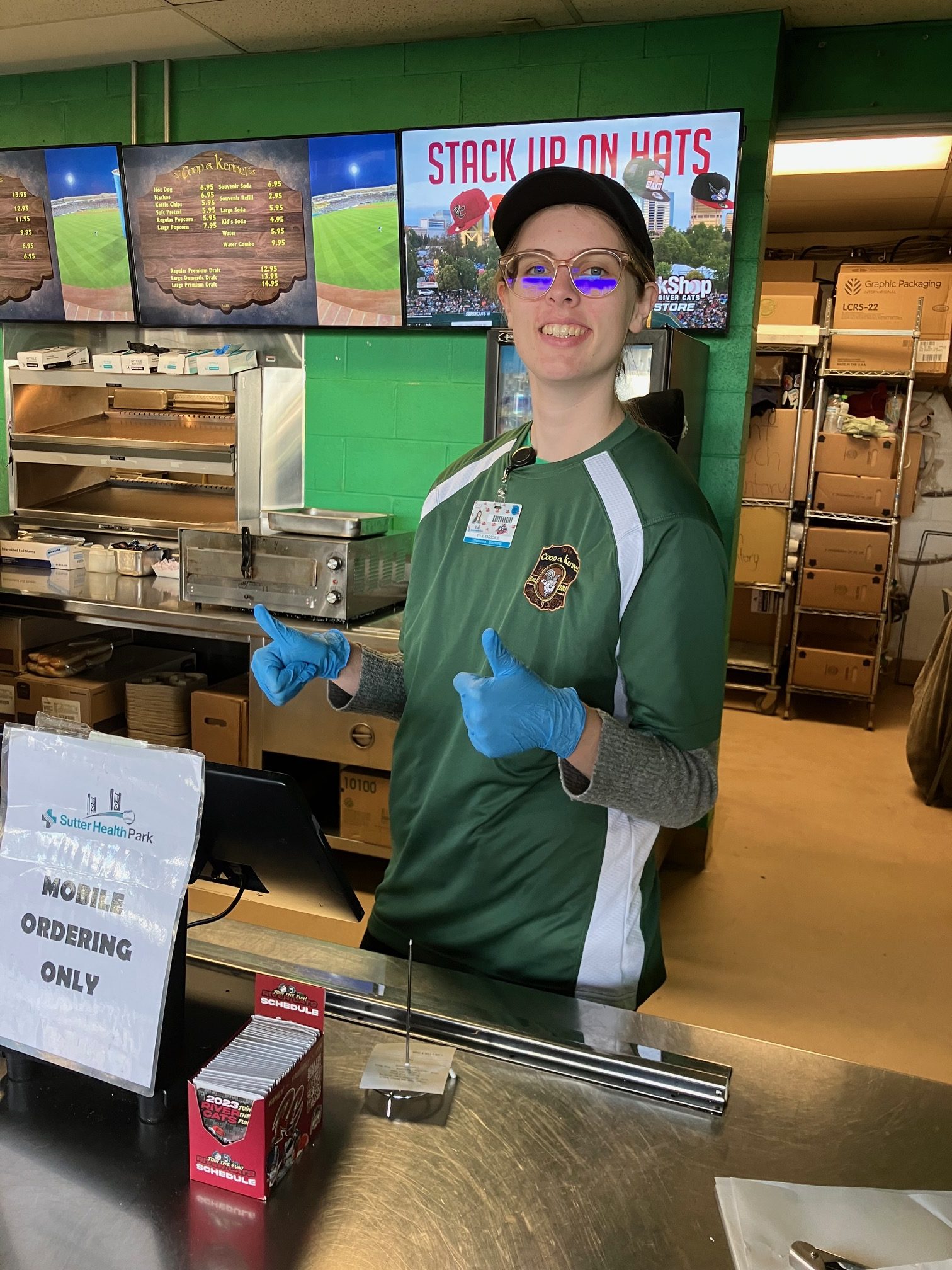 Student working customer service behind a food stall counter at a RiverCats game.