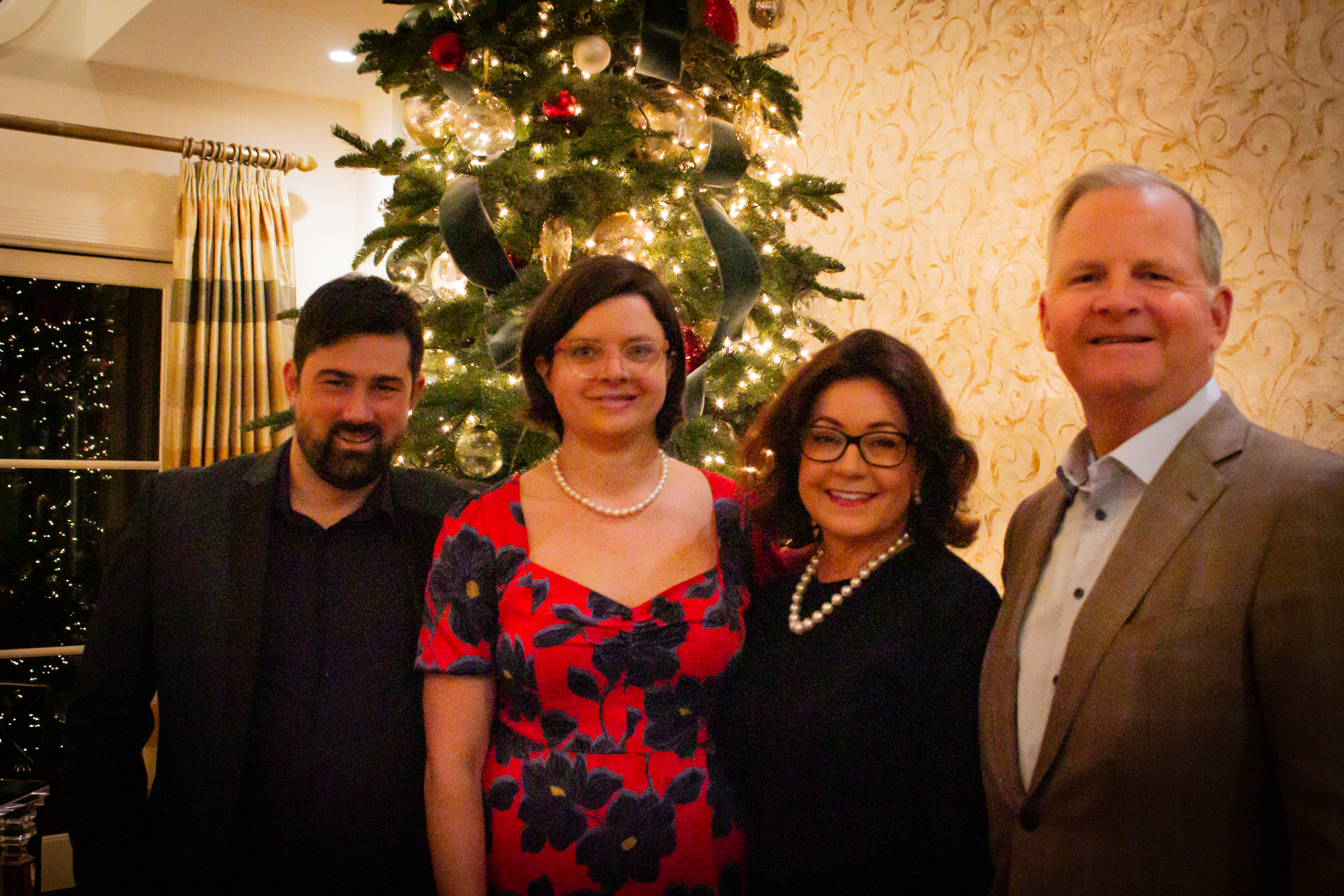 Erin Schirm, Caroline Eggert, Pam Eggert, and Steve Eggert smile in front of a christmas tree at a reception hosted at the Eggert home on Tuesday, December 12, 2023